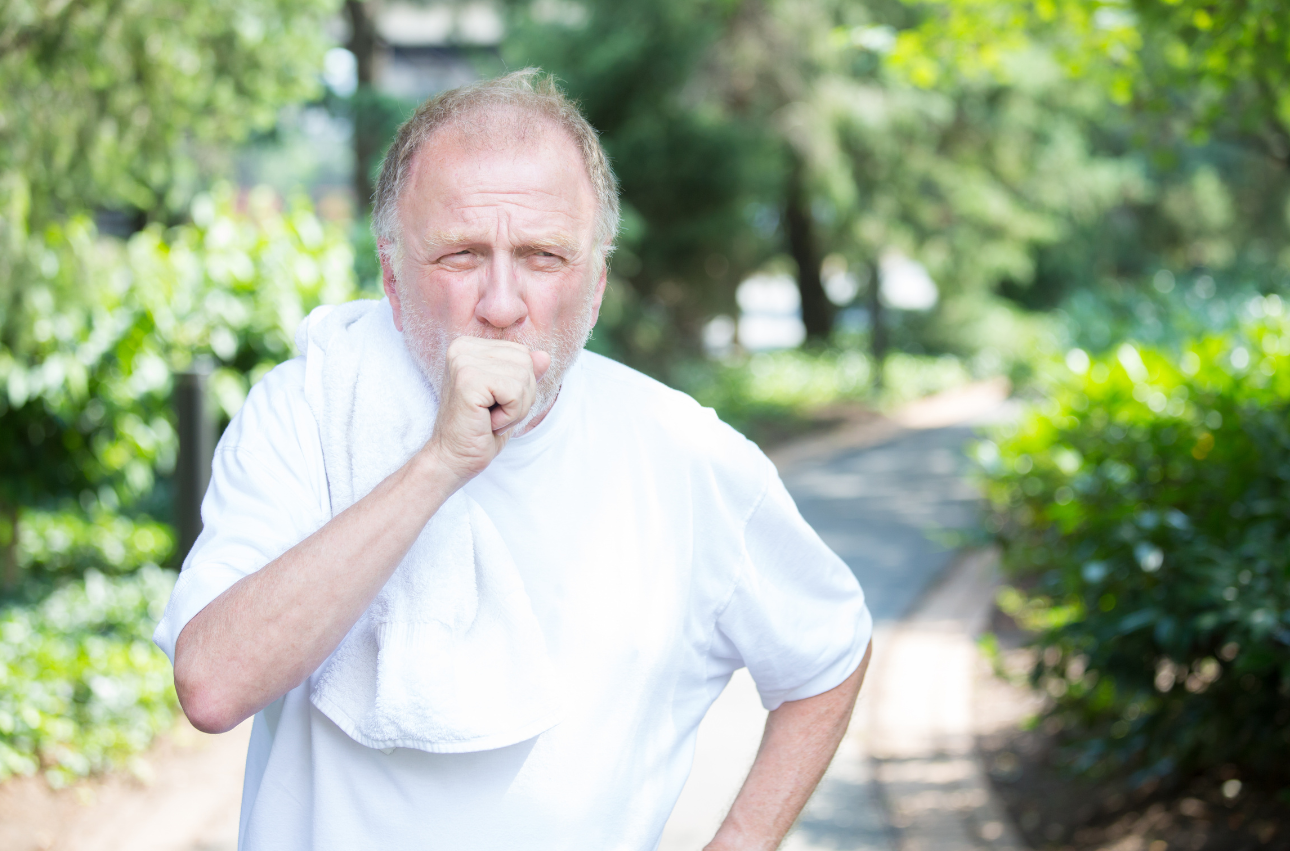 Elderly man coughing while walking outdoors, showing a common symptom of COPD.