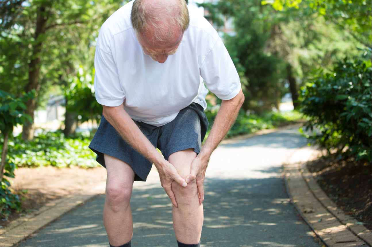 Senior man holding his knee in pain during a walk, indicating joint discomfort.