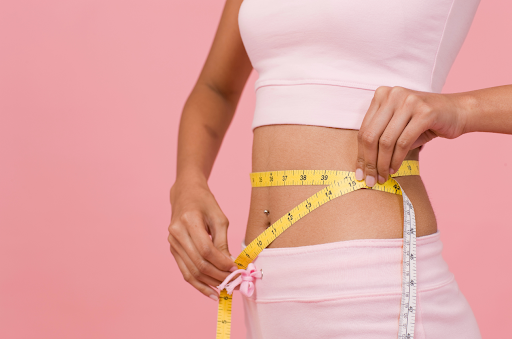 Woman measuring her waist with a tape measure, emphasizing weight loss and fitness.