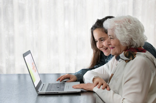 A young woman and an elderly woman smiling at a laptop, illustrating the role of education in COPD care.