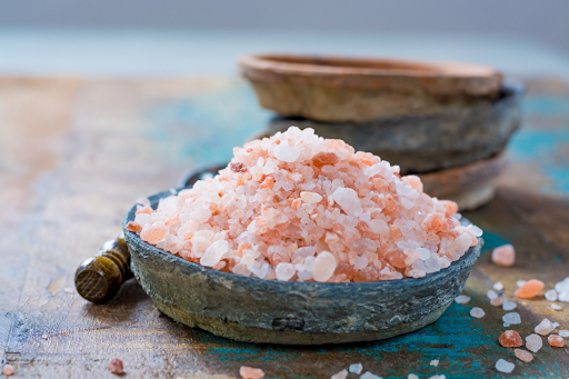A bowl filled with coarse pink Himalayan salt crystals on a rustic wooden surface, used for respiratory therapy.