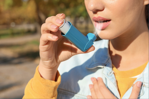 A woman using a blue inhaler, inhaling medication to relieve breathing difficulties.