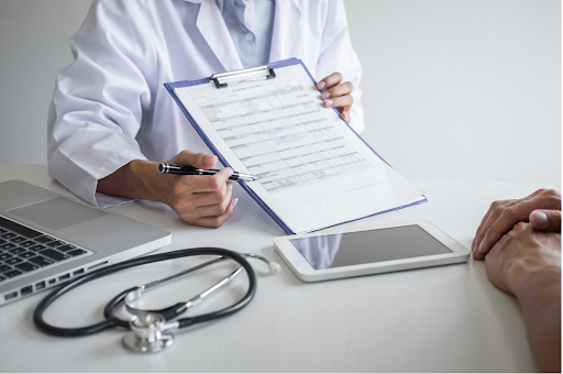 Doctor holding a clipboard with a stethoscope and a tablet on the table, consulting a patient.