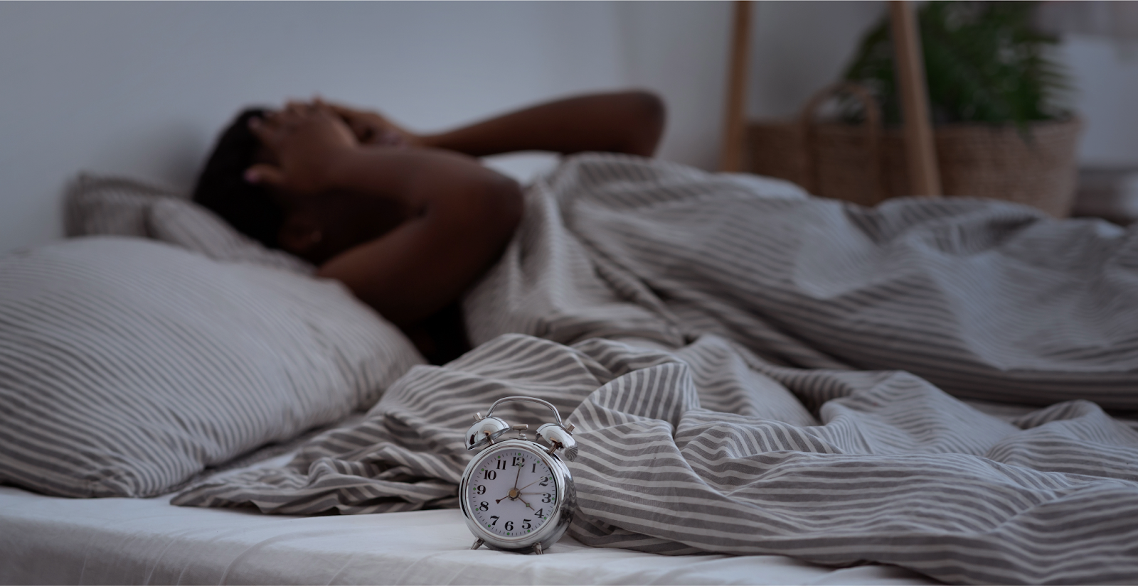 Person lying in bed struggling to sleep with an alarm clock on the bed